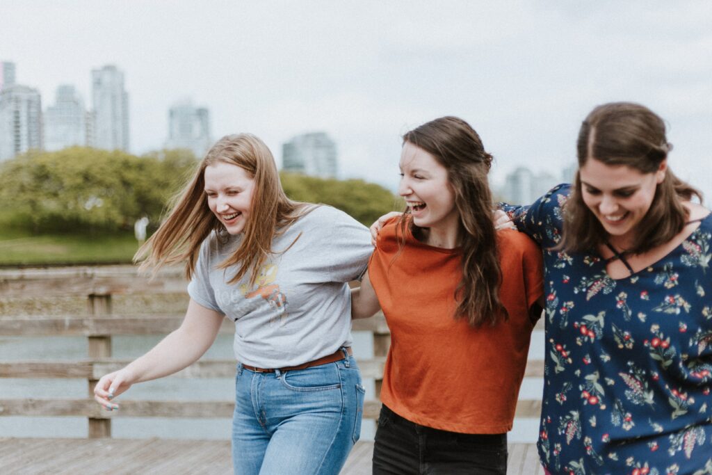 Emerging Adulthood drei lachende junge Frauen Arm in Arm.