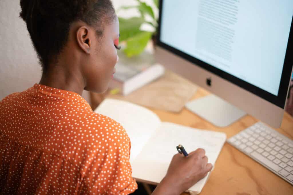 Frau Sitzt am Schreibtisch und schreibt in ein Notizbuch. Wissenschaftliche Texte schreiben