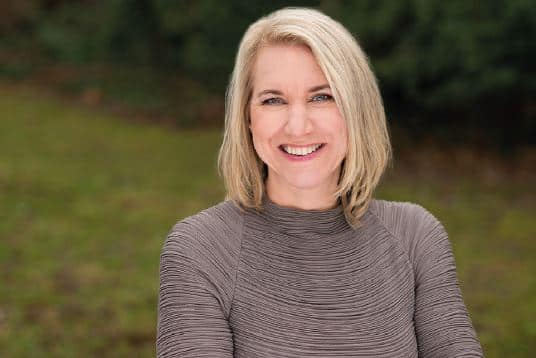 Frau mit blonden Haaren und braunem Pullover auf einer Wiese