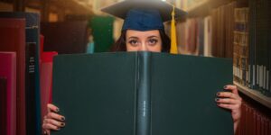 Junge Frau in Bibliothek schaut über den Rand eines grünen Buchs