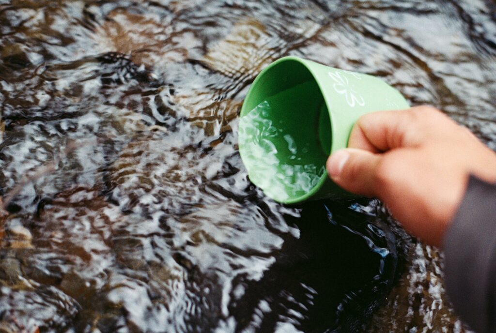 Person schöpft Wasser mit Becher. VG Wort