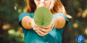Person holding green leaf into camera, presenting enhanced sustainibility measures